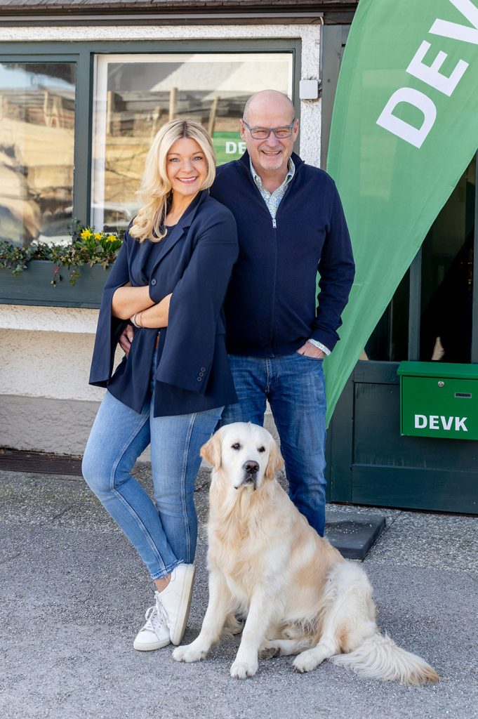 Michaela Wolkersdorfer posiert mit ihrem Vater und ihrem Hund vor ihrer DEVK-Geschäftsstelle. Sie und ihr Vater tragen Jeans und dunkelblaue Oberbekleidung. Der Hund ist ein Golden Retriever.