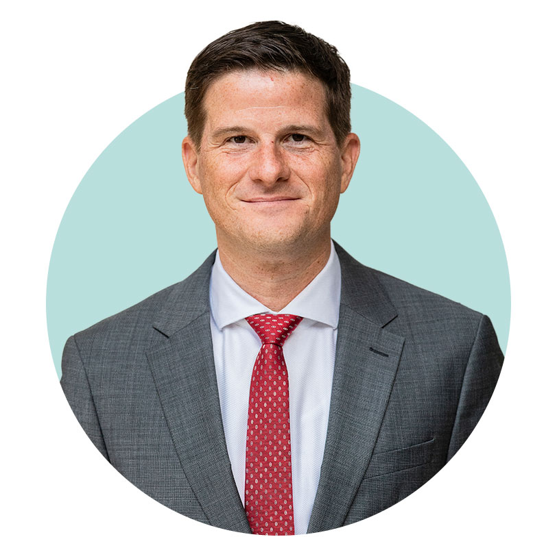 Porträt von Dr. Michael Zons, ein Mann mit braunem Haar und Business-Kleidung. Er trägt ein dunkelgraues Jackett und ein weißes Hemd mit rot-gemusterter Krawatte.