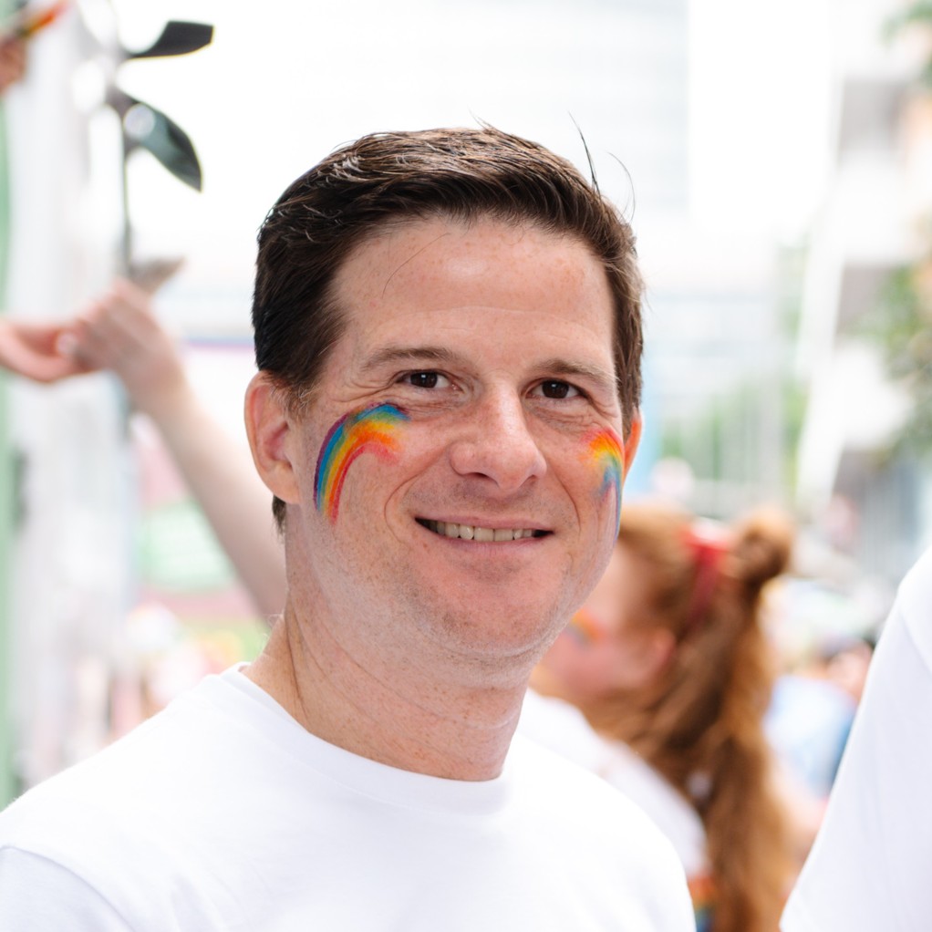 Hier sieht man einen strahlenden Mann mit Regenbogen-Farben im gesicht