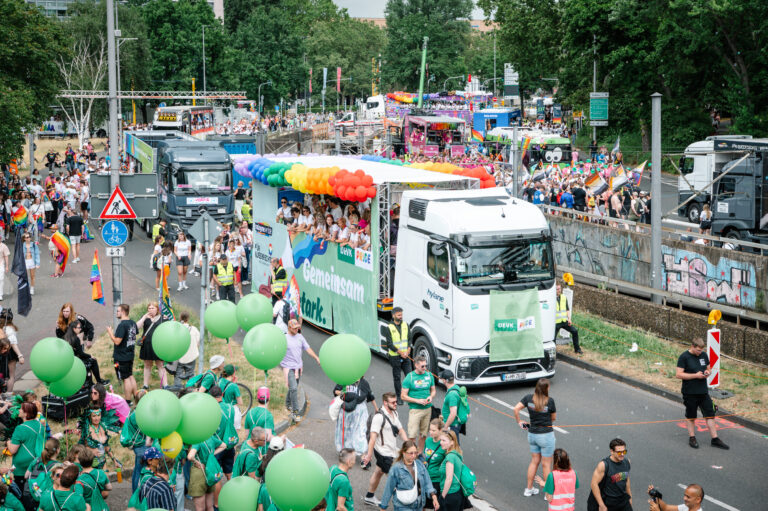 Ein Truck mit vielen Ballons behangen und grünen Werbeträgern fährt durch die Menge