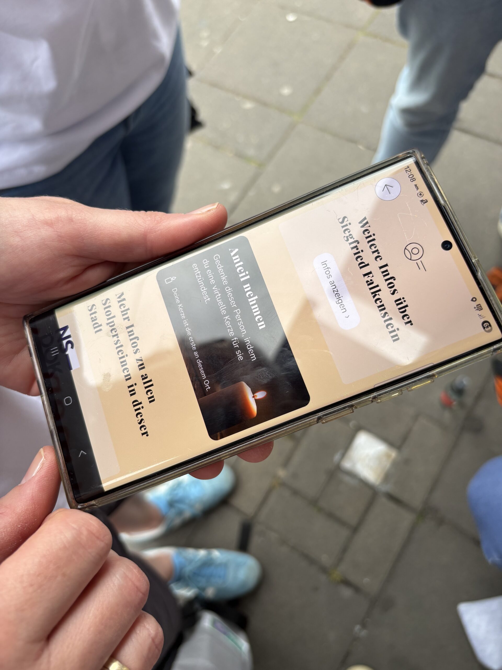 Auf einem Mobiltelefon in Frauenhänden ist die Stolpersteine-App des WDR zu sehen und die Funktion, mit der man digital eine Kerze zum Gedenken anzünden kann.